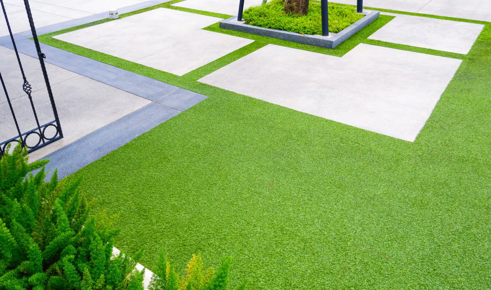 Artificial turf lawn bordering large concrete pavers around a tree planter in a front yard